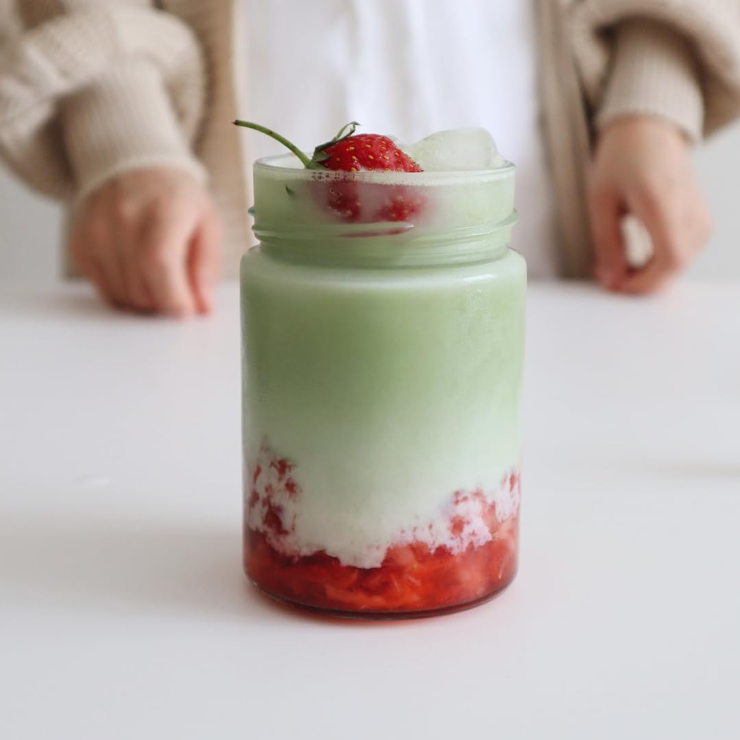 Matcha tea powder smoothie with strawberries in a jar on a white surface